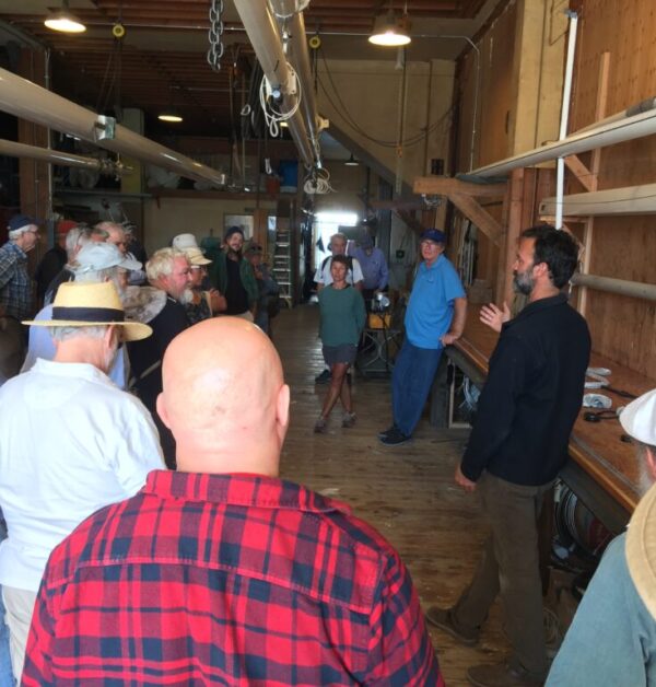 Group of people gathered to listen to a presentation in the Brion Toss Yacht Rigging loft in Port Townsend during the 2022 Wooden Boat Festival.